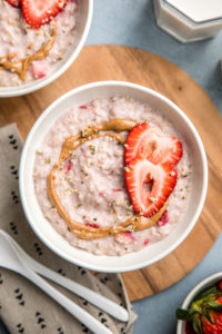close up photo of strawberries and cream oatmeal in white bowl topped with almond butter and fresh strawberries