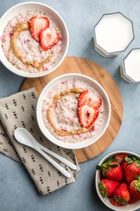 two bowls of strawberries and cream oatmeal with almond milk and fresh strawberries