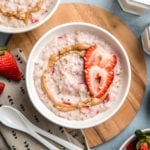 strawberries and cream oatmeal topped with almond butter and hemp hearts in white bowl on blue background