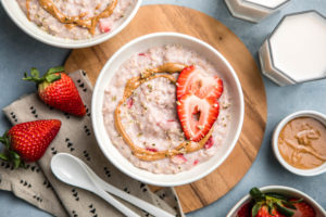 strawberries and cream oatmeal topped with almond butter and hemp hearts in white bowl on blue background