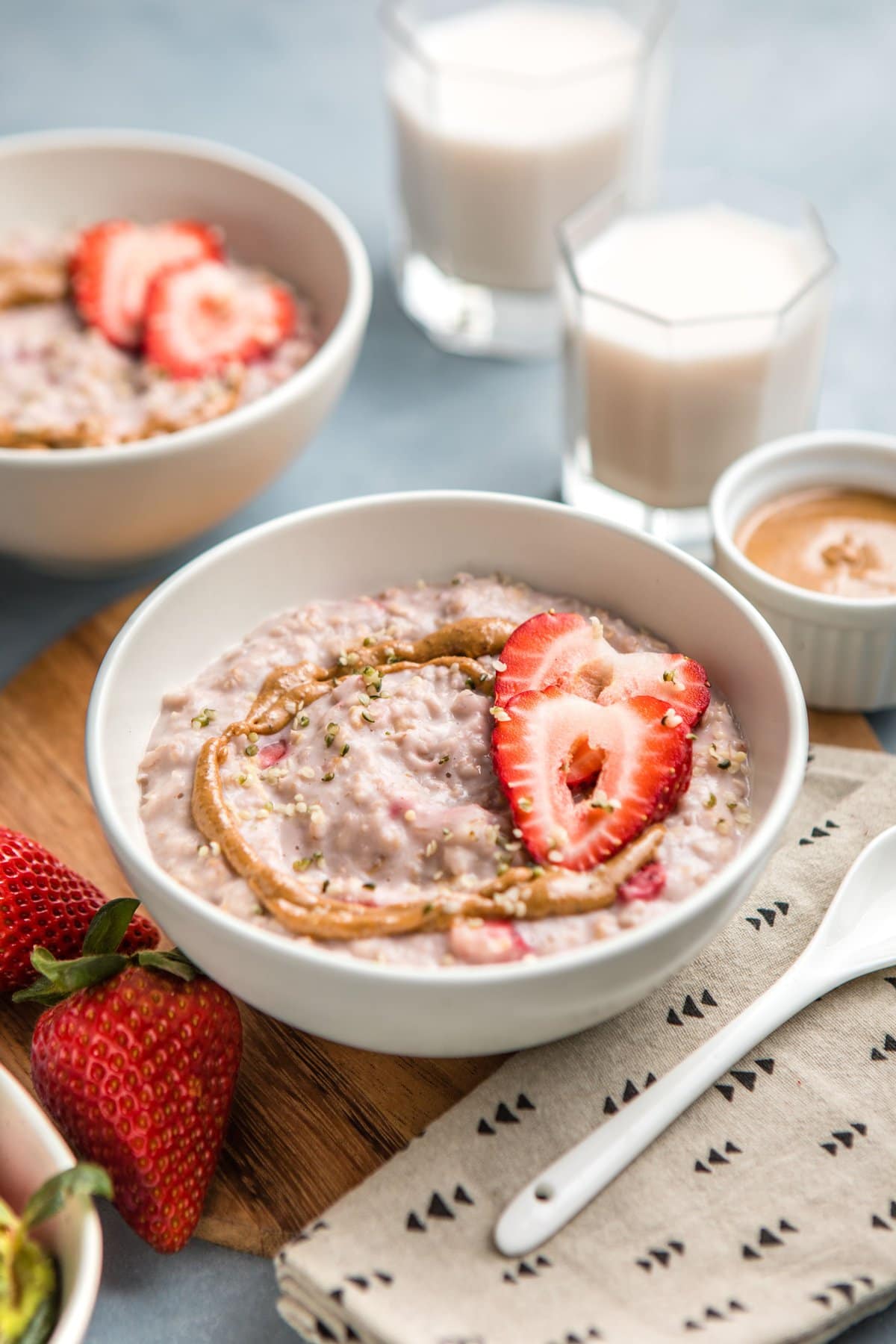 angled shot of white bowl of strawberries and cream oatmeal with glass of almond milk