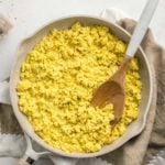 tofu scramble in large white pan with wooden spoon on light gray background