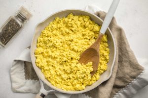 tofu scramble in large white pan with wooden spoon on light gray background