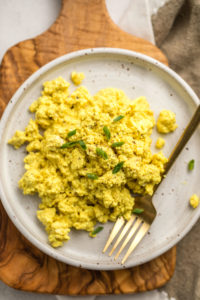 tofu scramble topped with fresh chives on white speckled plate with gold fork