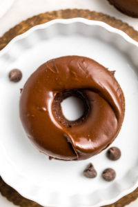 close up photo of chocolate covered donut on white plate with chocolate chips