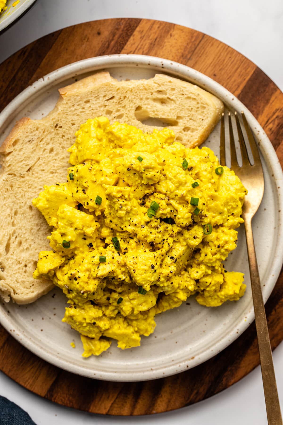 tofu scramble served on a plate with a slice of bread on the side, topped with chives and more seasoning