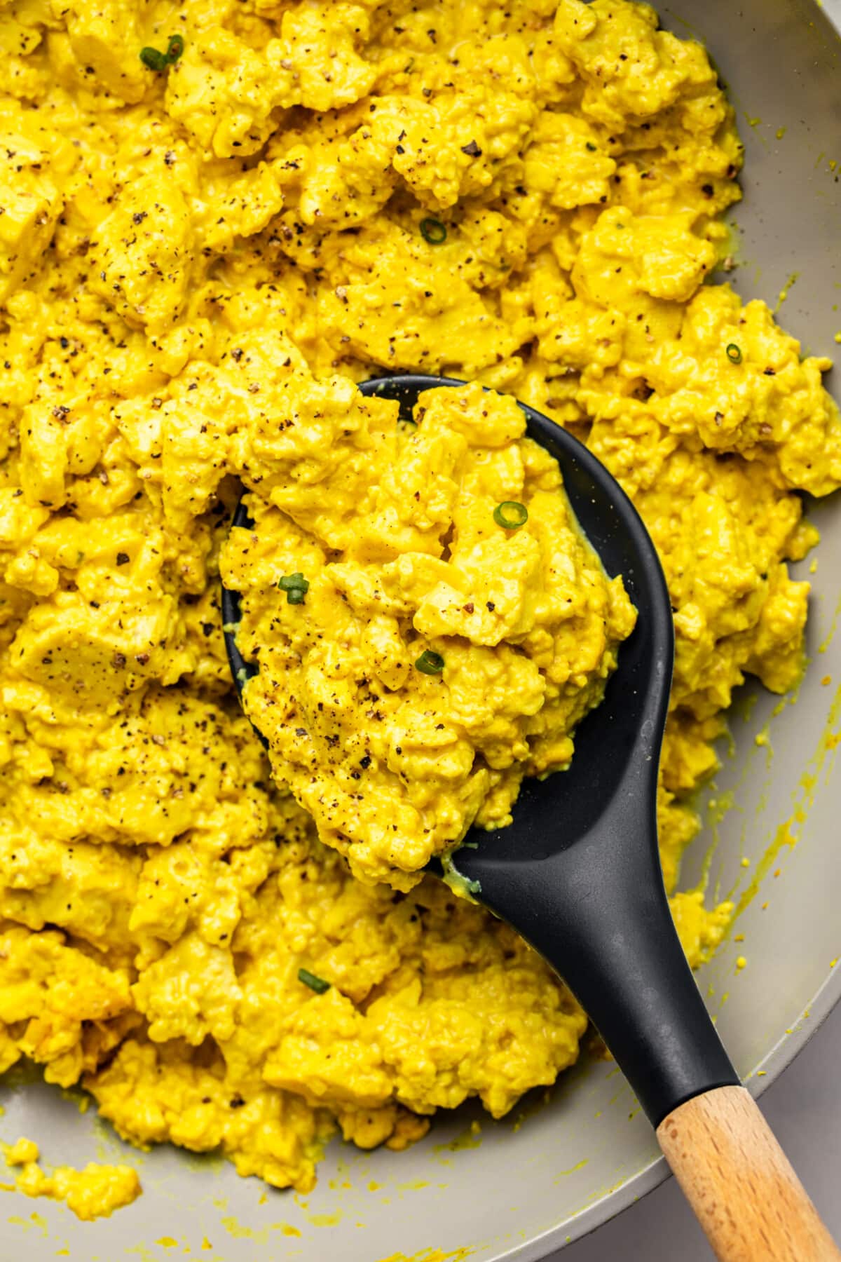 a serving spoon scooping up vegan tofu scramble from the pan