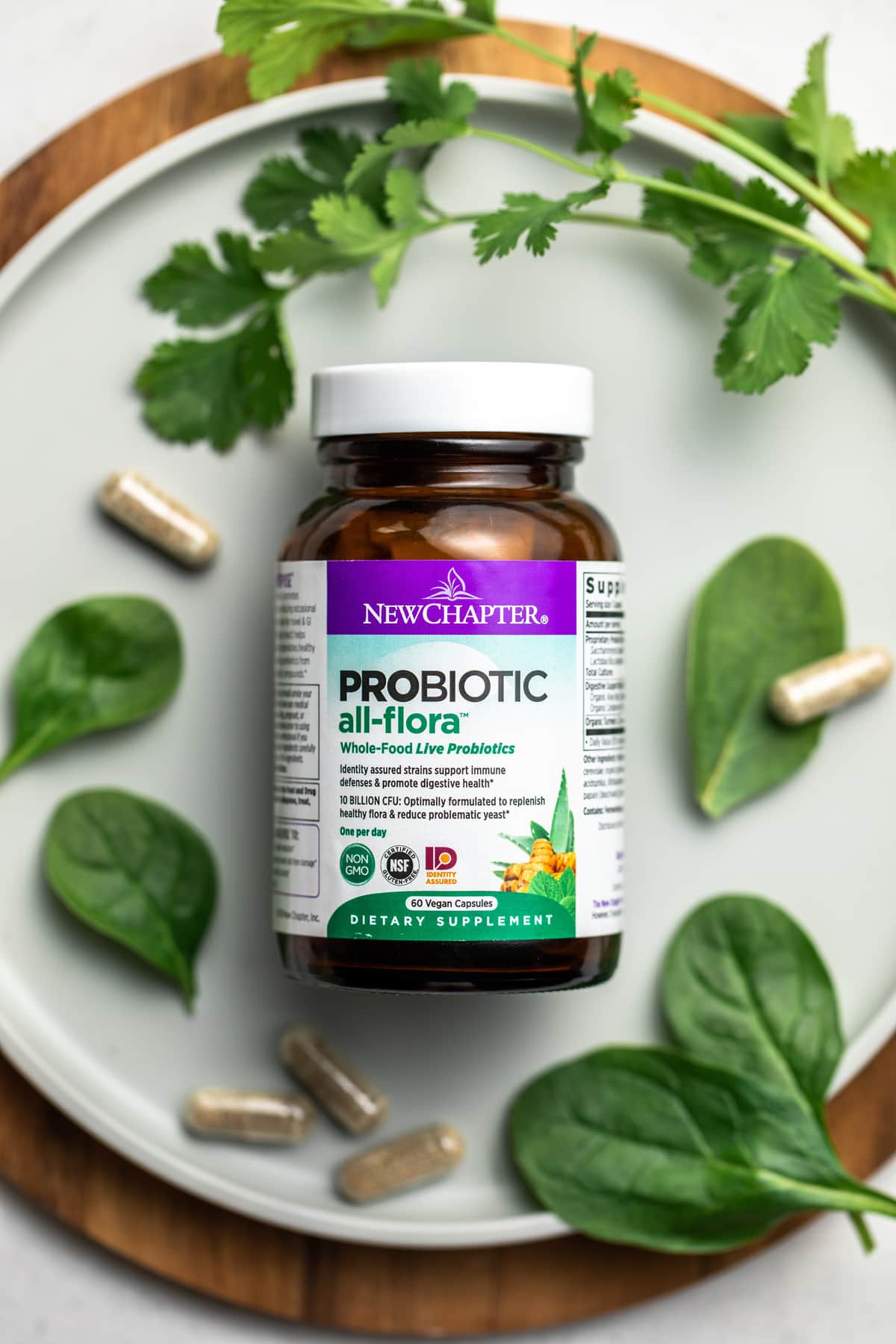 bottle of new chapter probiotics with pills on round cutting board with spinach and cilantro