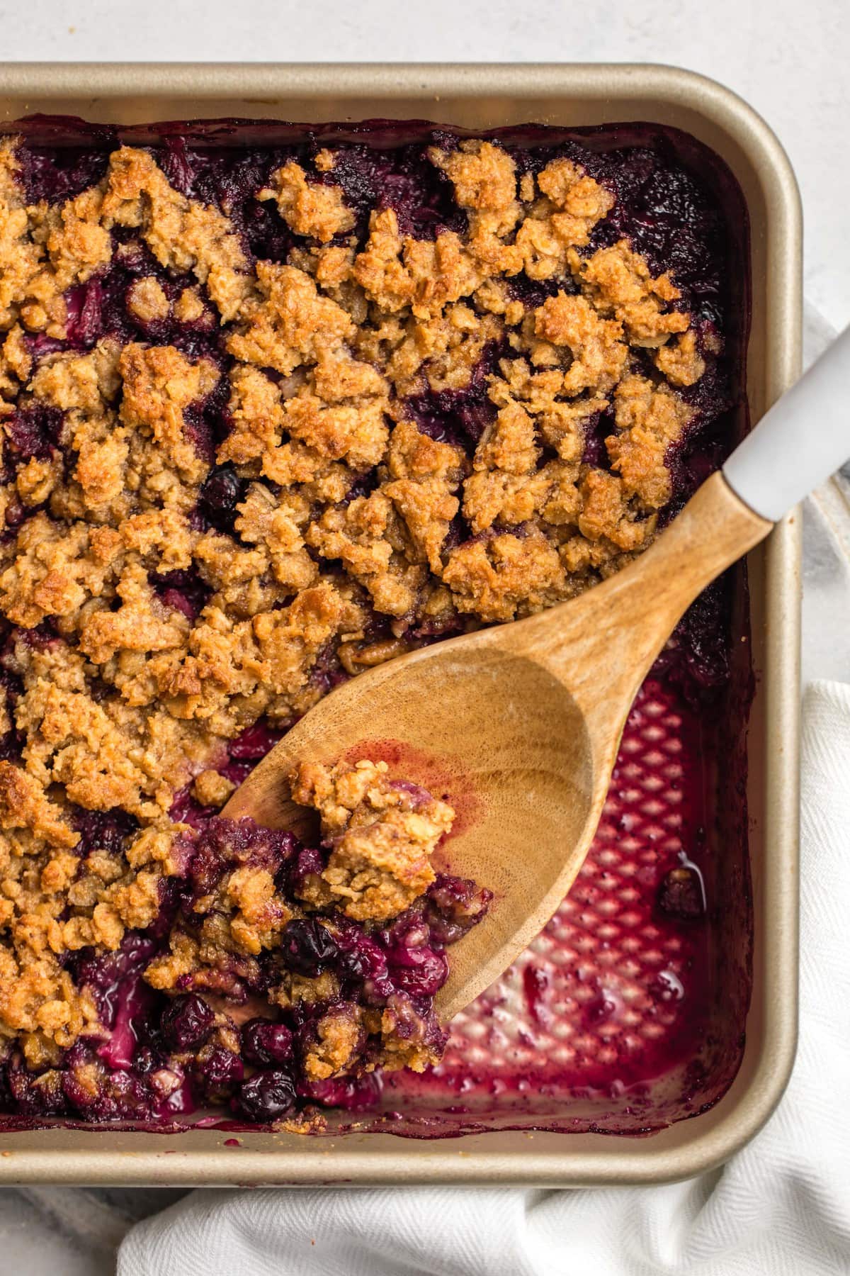 baked berry crumble in gold dish with wooden spoon