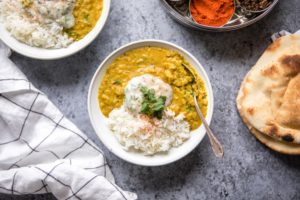 Two bowls of dal tadka with rice and raita on gray background