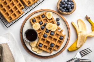 vegan blender waffles on small white plate with blueberries, banana, and maple syrup