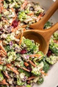 close up photo of broccoli salad with wooden serving spoons in white bowl