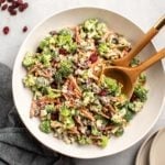 large white bowl of broccoli salad with wooden serving spoon and tan plates