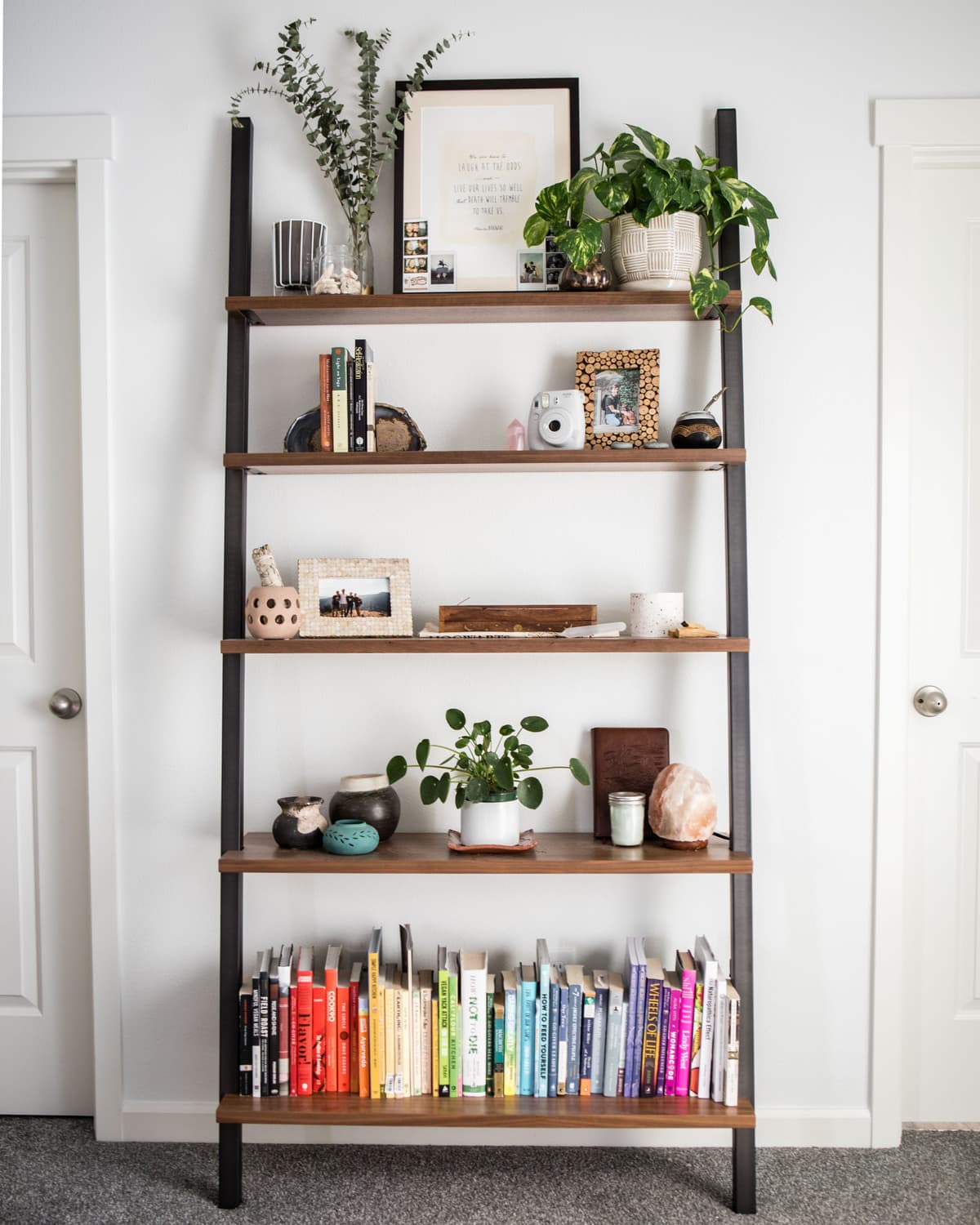 photo of leaning wood and metal bookshelf decorated with rainbow books and various mementos