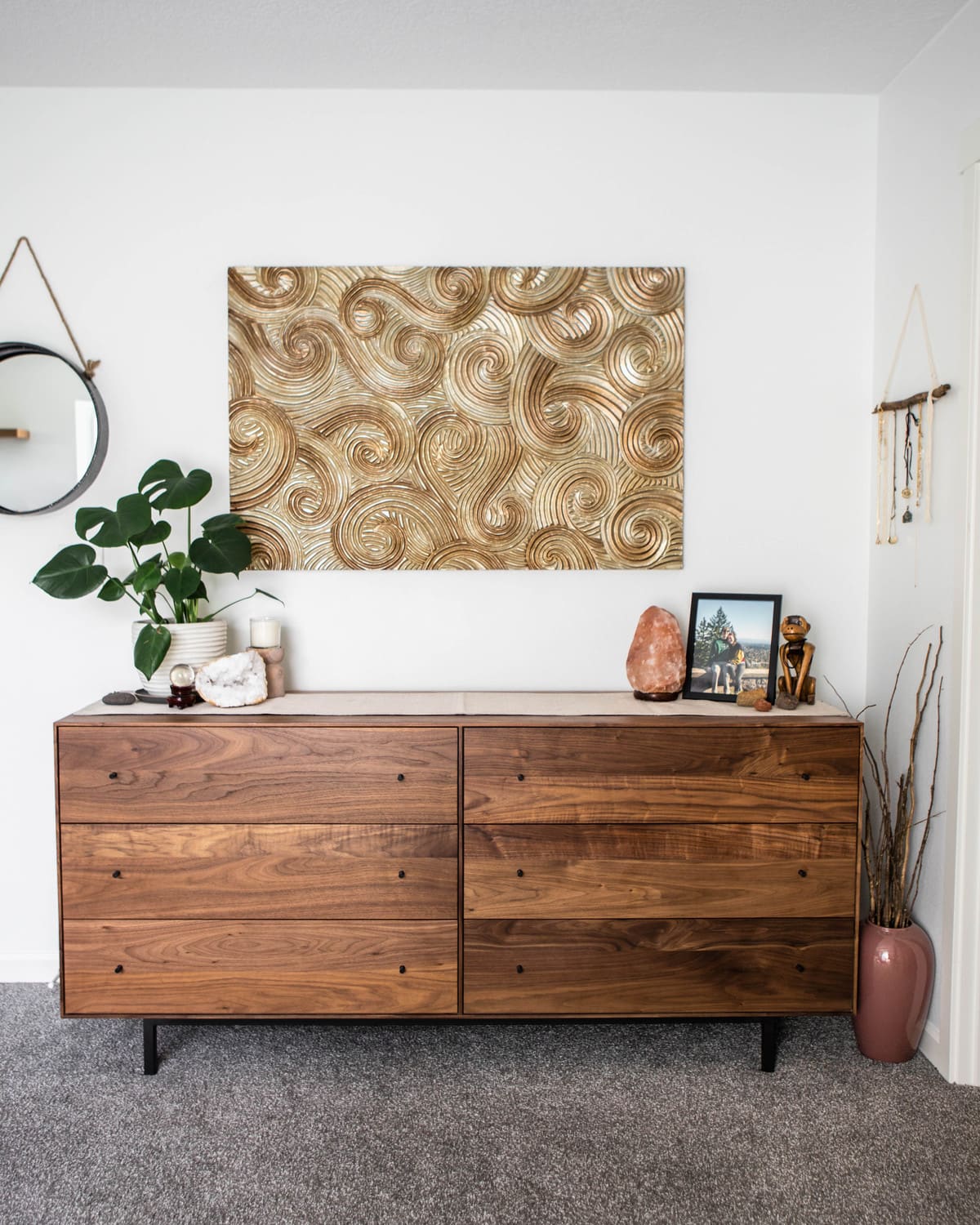 long wooden dresser decorated with pictures, a monstera plant, and gold art collage