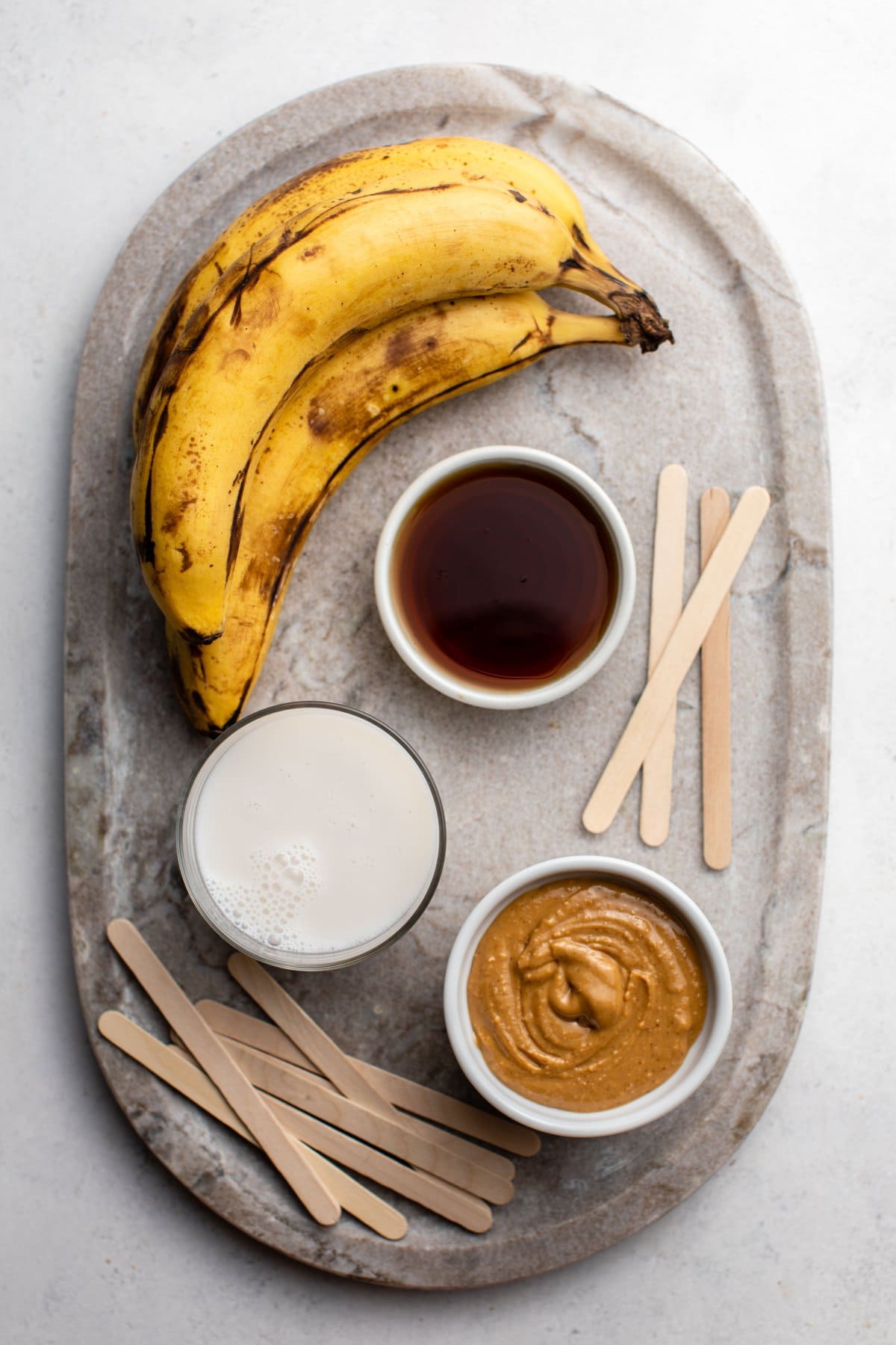 ingredients for peanut butter banana popsicles on stone serving board
