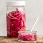 large mason jar and small glass dish of pickled red onions on wood cutting board