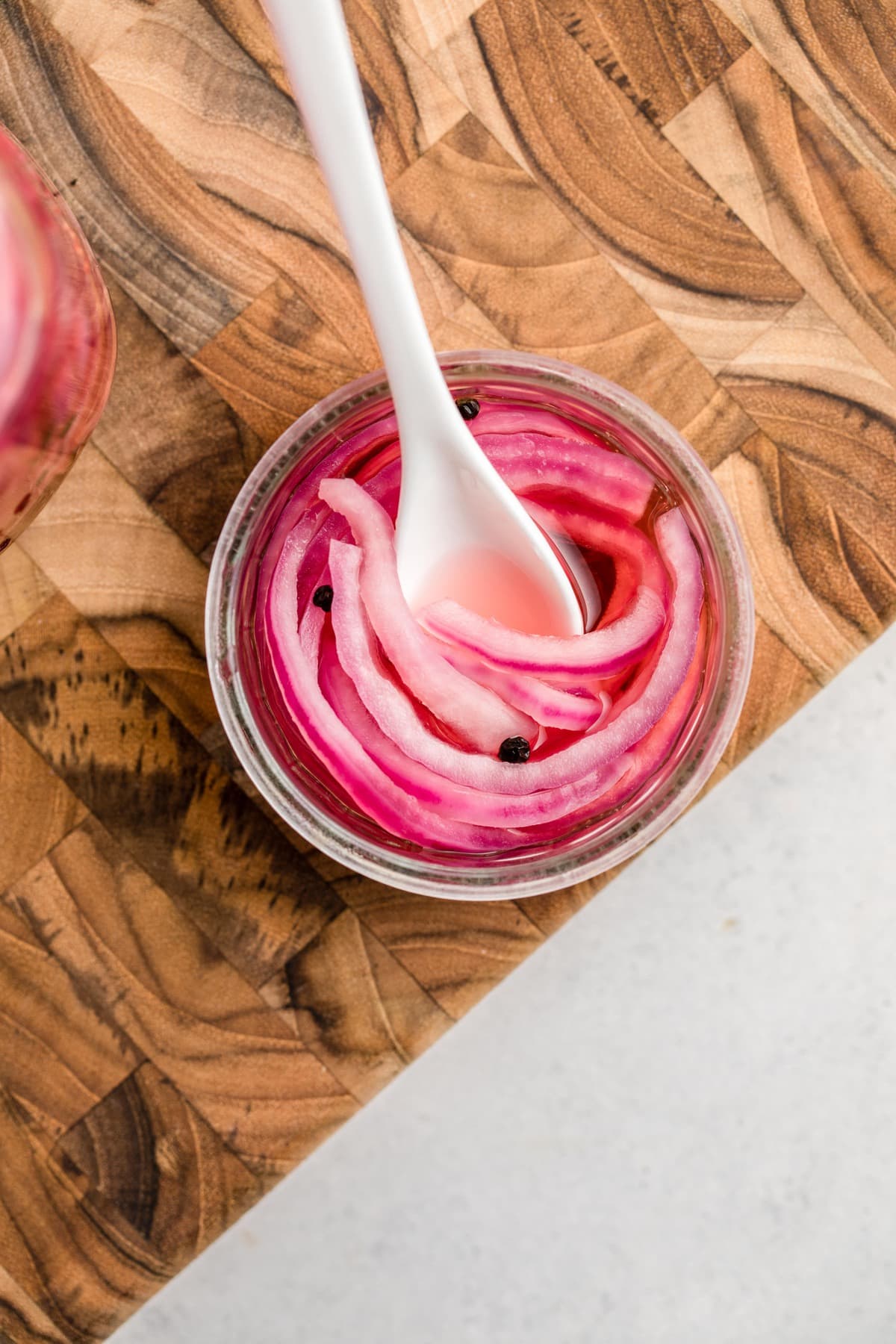small glass dish of pickled red onions with white spoon on wood cutting board