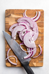 knife with sliced red onion on wood cutting board