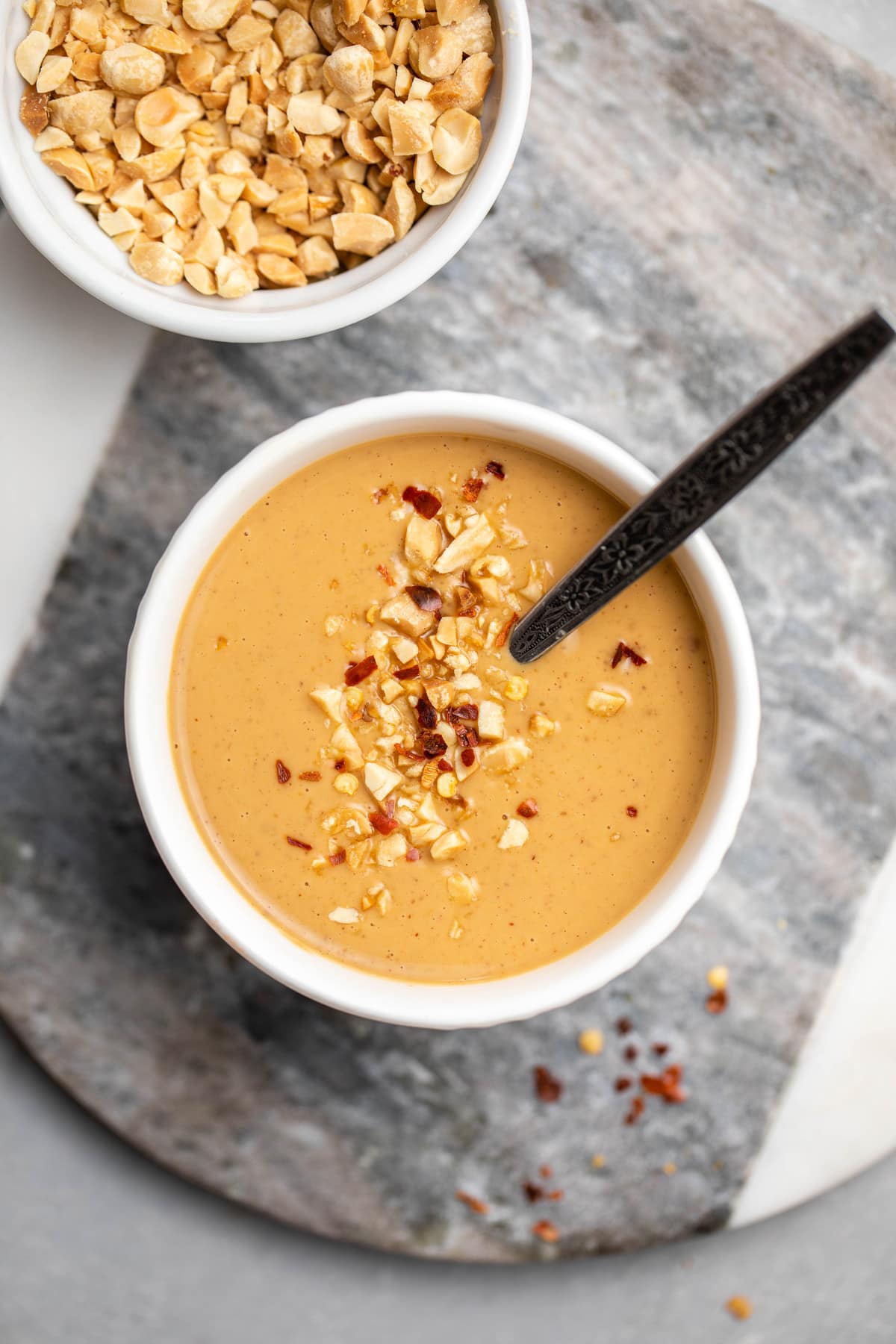 peanut sauce topped with chopped peanuts and chili flakes in small white bowl