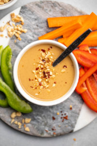 peanut sauce in white bowl with chopped peppers and carrots