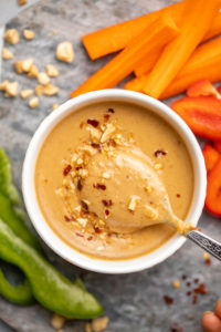 white bowl of peanut sauce topped with chili flakes with spoon mixing