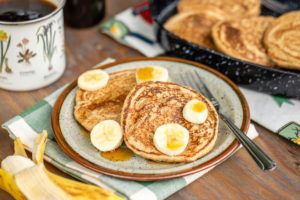 two pancakes topped with bananas and maple syrup on tan speckled plate