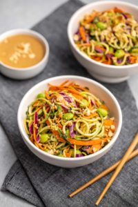 angled shot of two white bowls of zucchini noodle salad with peanut sauce and wooden chopsticks