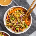 white bowl of zucchini noodle salad with peanut sauce and chopticks on dark grey linen background