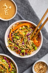 white bowl of zucchini noodle salad with peanut sauce and chopticks on dark grey linen background