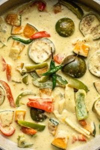 close up photo of cooked thai green curry in grey pot with two thai green chilis on top