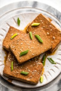 braised tofu on white plate topped with green onion and sesame seeds