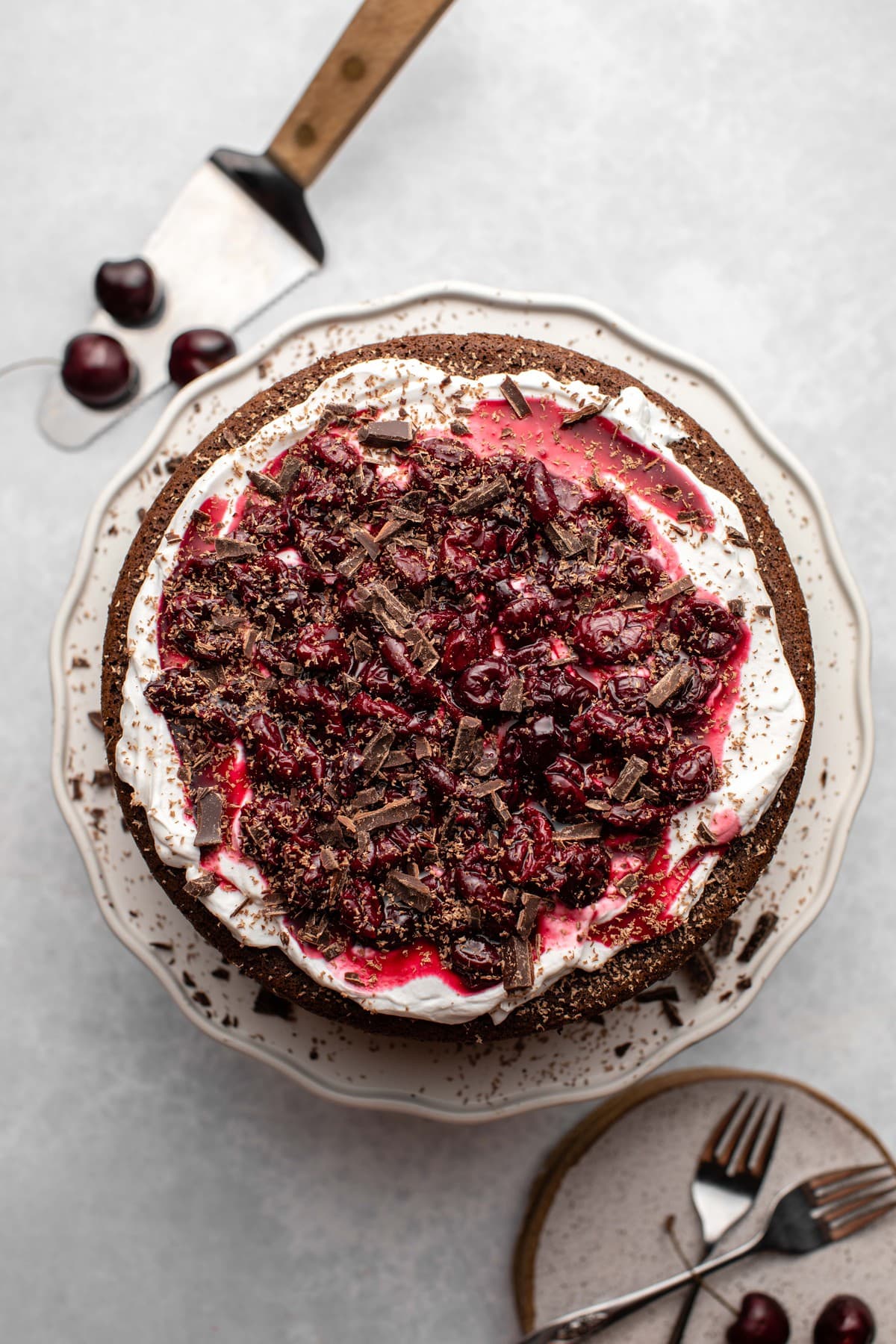 whole chocolate cake topped with cherries and coconut whipped cream on white cake stand