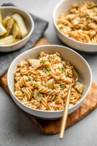 two white bowls of dill pickle pasta salad with side of pickles and navy napkin