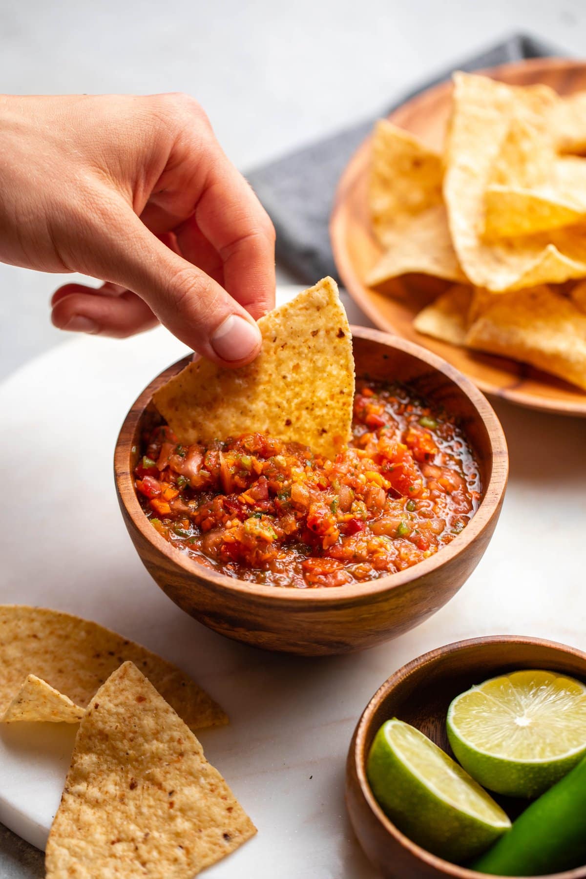 hand dipping tortilla chip into wooden bowl of salsa