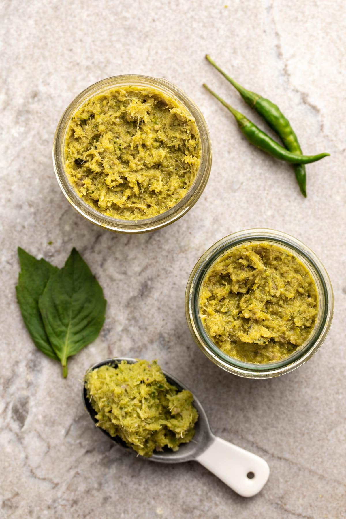 three jars of thai green curry paste on grey stone background