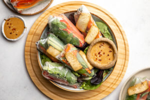 bowl of rice paper rolls with peanut sauce on wood cutting board