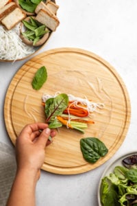 hand putting herbs into rice paper roll on wood cutting board