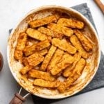 bbq tempeh in white cooking pan with bowl of bbq sauce and wooden spoon