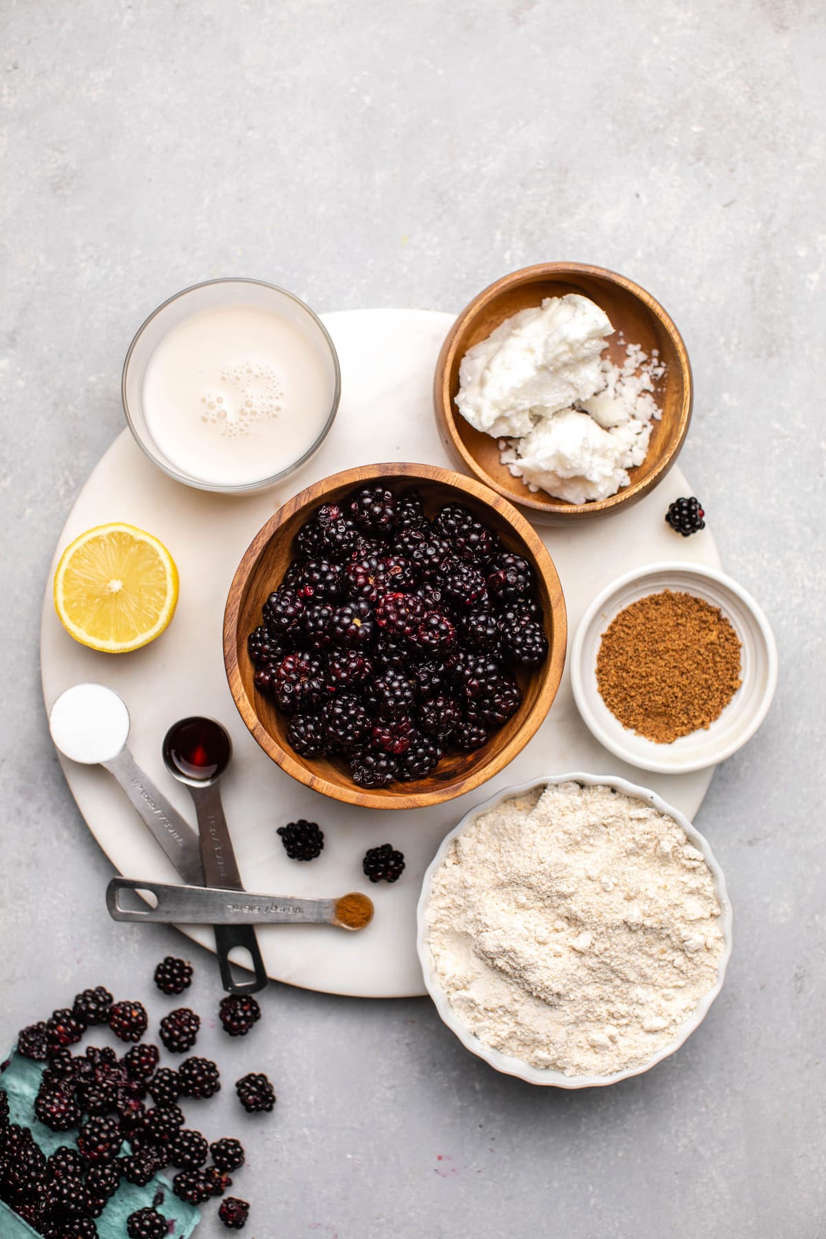 ingredients for blackberry cobbler arranged in small bowls on round white cutting board
