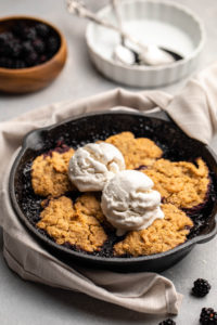blackberry cobbler in small cast iron skiller topped with two scoops of vanilla ice cream