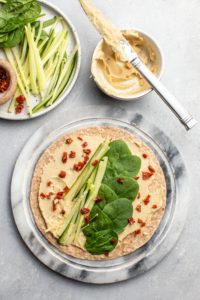 marble cutting board filled with hummus, cucumber, sundried tomato, and spinach on tortilla
