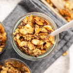 close up photo of small glass jar of granola with white spoon