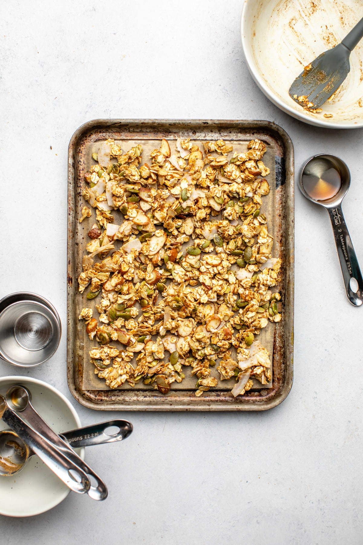 granola spread on small baking tray with empty measuring cups around it