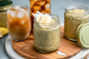 glass jars of thai tea overnight oats on wood serving tray with glass of thai tea in the background
