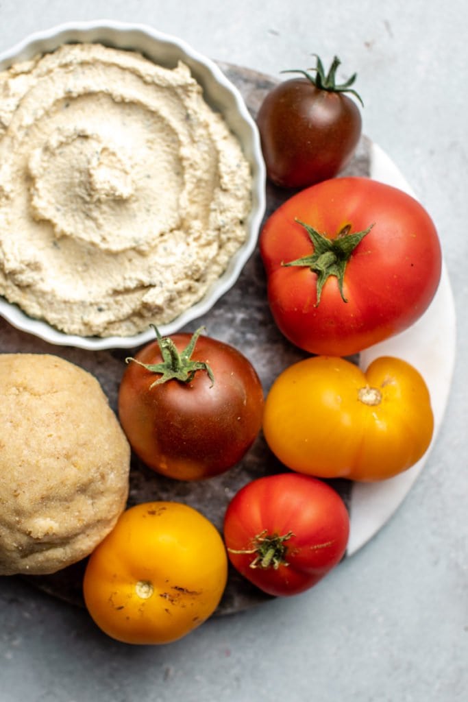 close up photo of tomatoes, dough, and ricotta cheese on marble cutting board