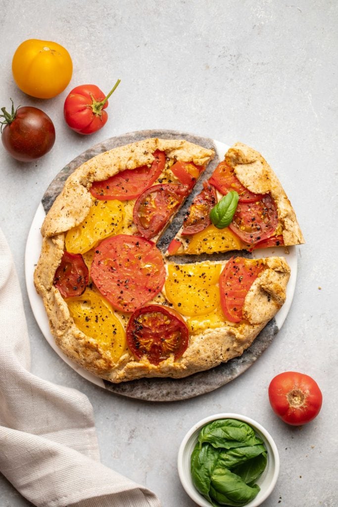 cooked tomato galette on round serving tray with gray linen and fresh tomatoes 