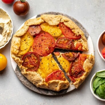 tomato galette on round serving board with fresh basil and tomatoes on the side