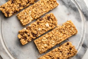 3 flavors of chewy granola bars arranged diagonally on a round marble cutting board
