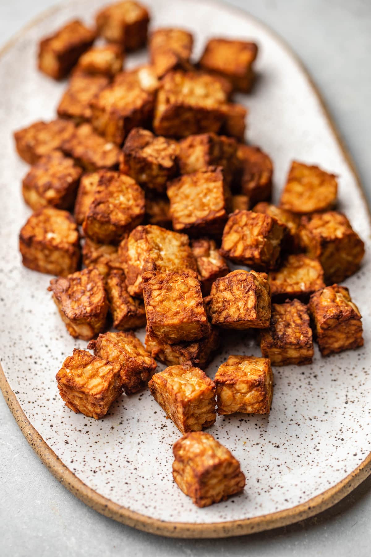 crispy tempeh pieces on white serving tray on grey background